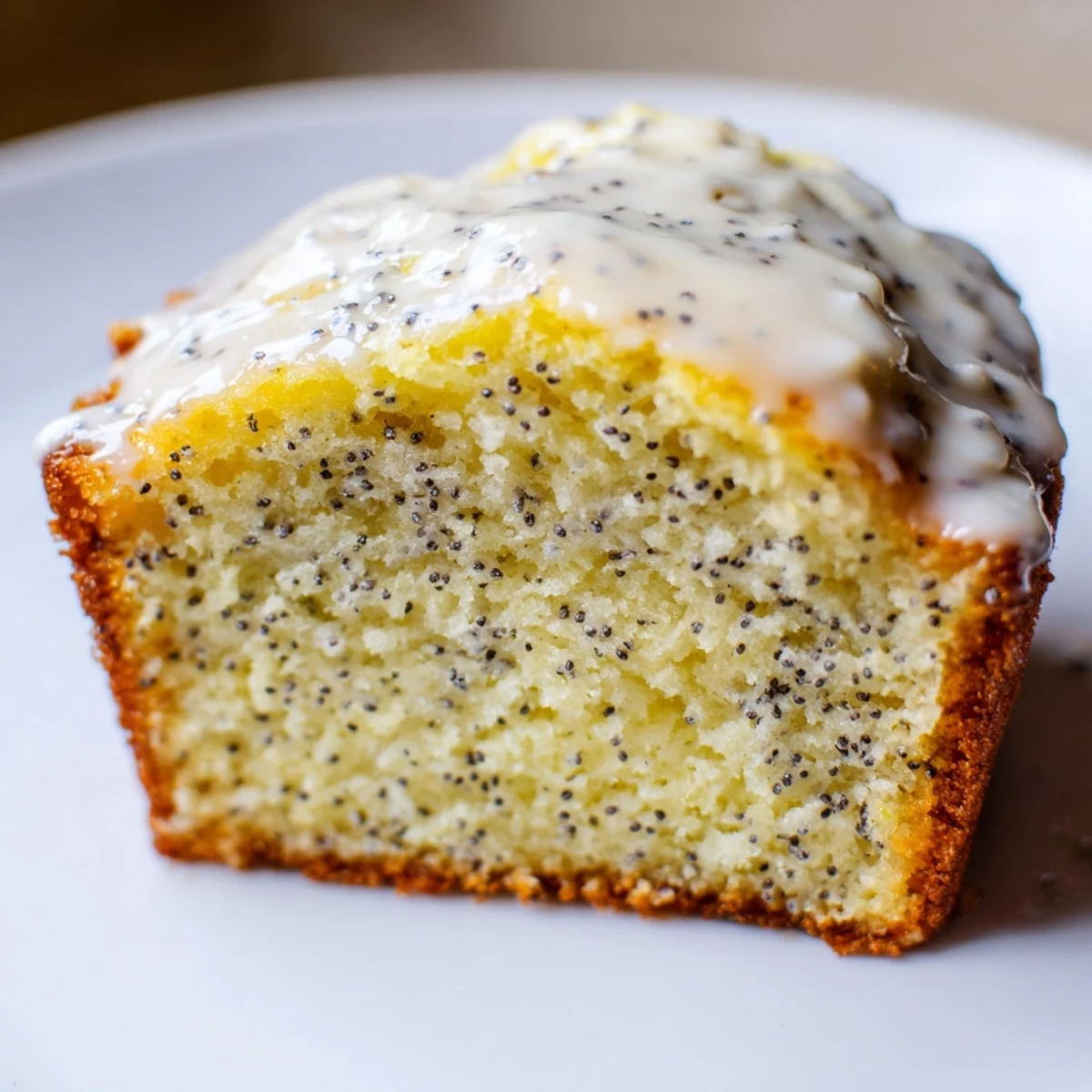 Golden-brown Lemon Poppy Seed Muffins with a glossy lemon glaze dripping down the sides, served on a white plate.