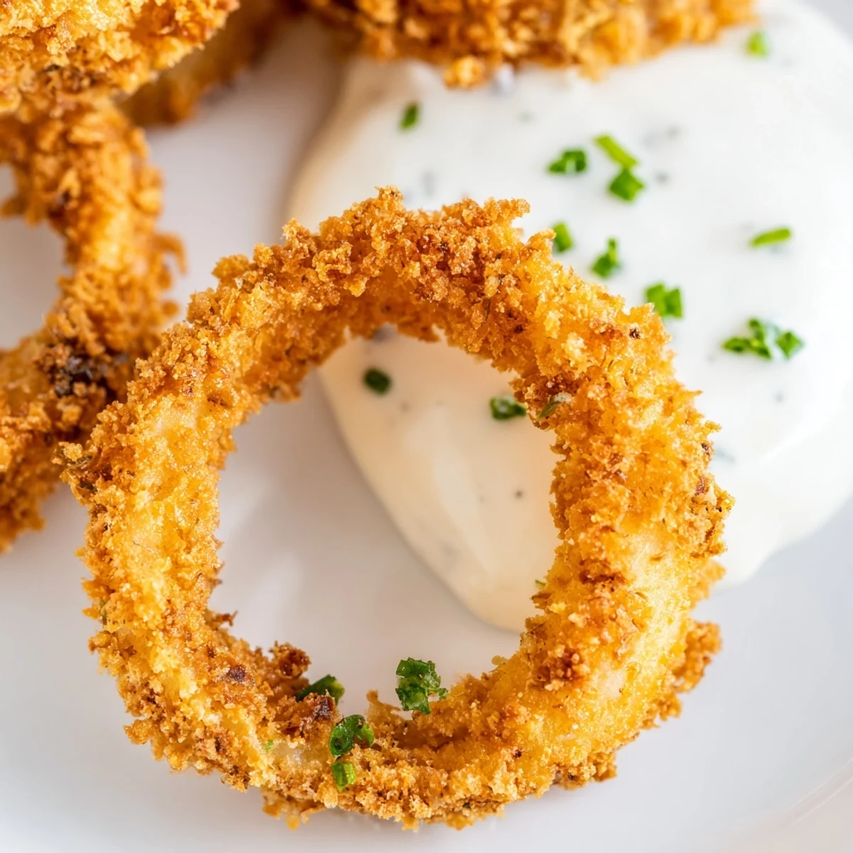 Golden Crispy Baked Onion Rings with Ranch Dressing on a plate, served next to a small bowl of creamy homemade dip.