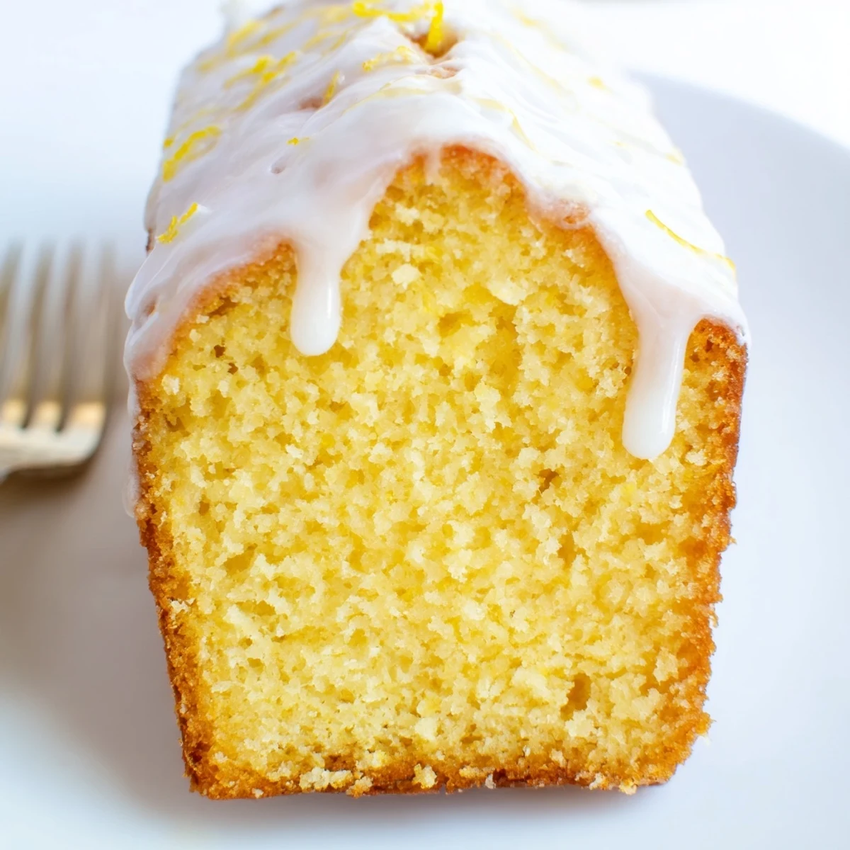 A freshly baked Lemon Loaf drizzled with tangy glaze, sliced to show tender crumb and bright lemon zest flecks.