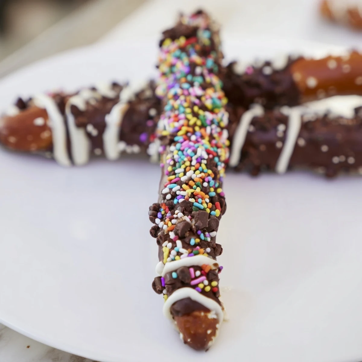 Homemade Chocolate Covered Pretzel Rods topped with festive sprinkles, stacked for a delicious snack gift.