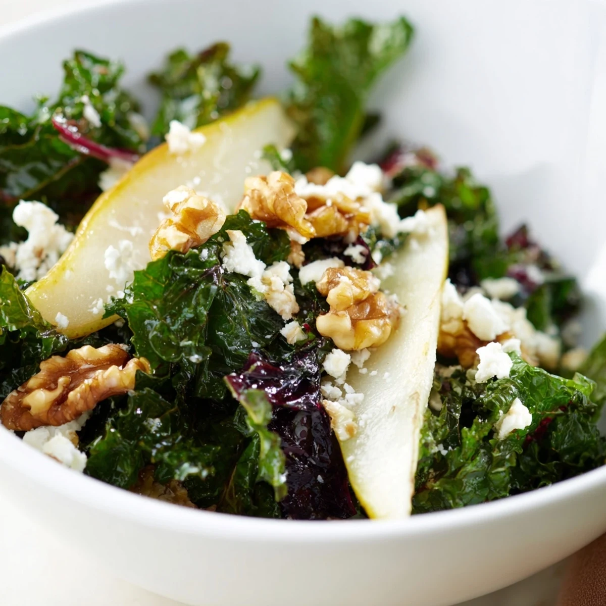 Freshly sliced pears and toasted walnuts top a vibrant Winter Green Salad with tangy vinaigrette, served on a white platter.