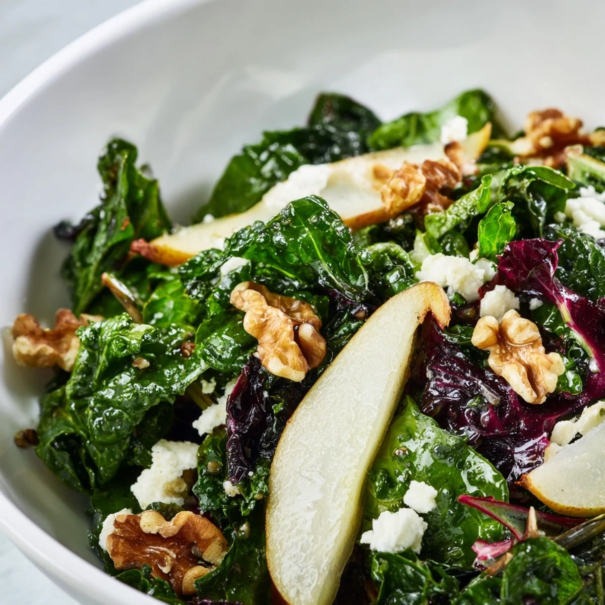 A close-up of the Winter Green Salad featuring shiny pear slices, toasted pecans, and fresh greens glistening with vinaigrette.