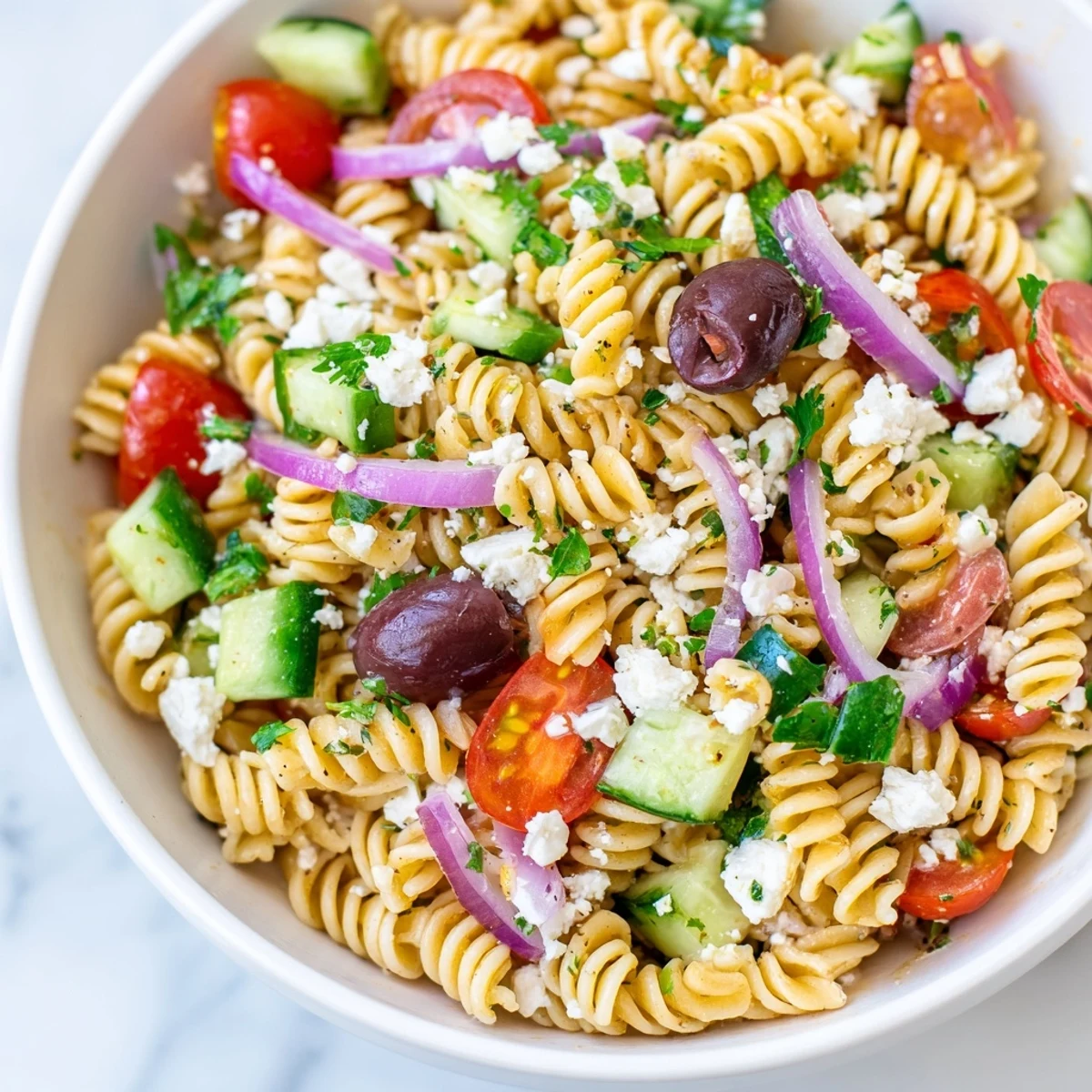 Ready-to-serve Mediterranean Pasta Salad with Olives and red onion, garnished with fresh parsley, perfect for a summer picnic or backyard barbecue.