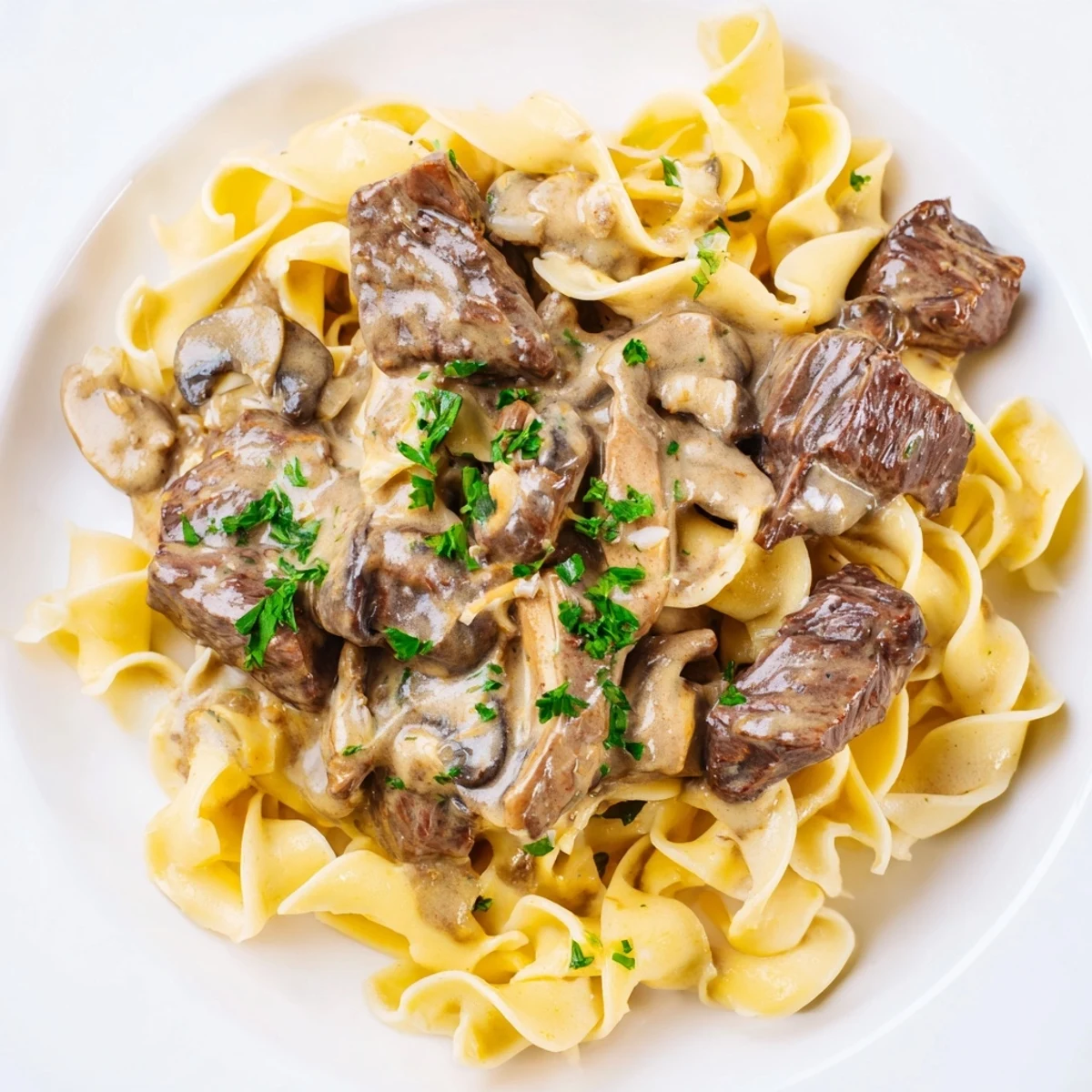 Creamy Beef Stroganoff over Egg Noodles with Mushroom Sauce served steaming hot on a white plate with fresh parsley garnish.