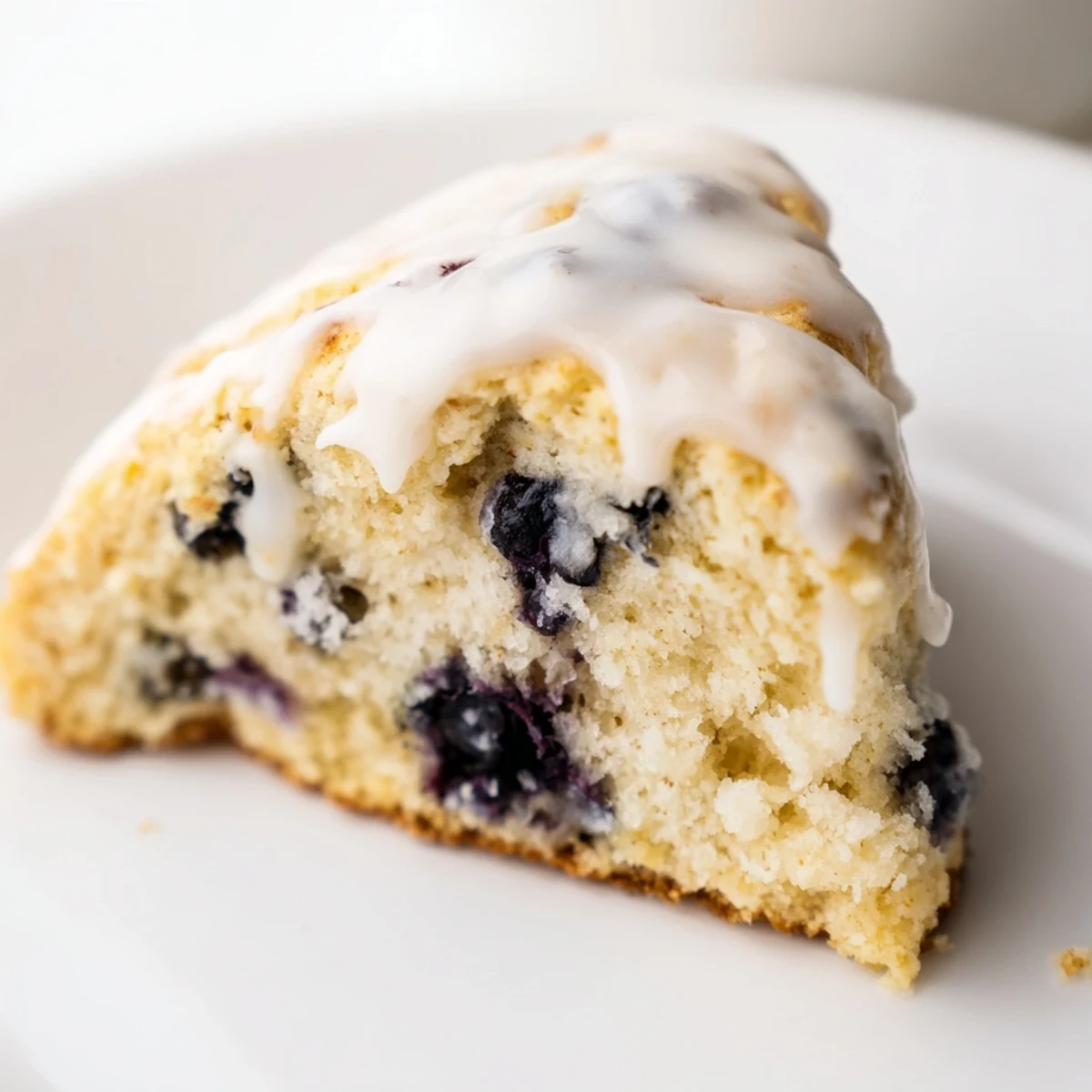 A close-up view of warm Lemon Blueberry Scones with Sweet Vanilla Glaze, revealing a tender crumb packed with juicy berries and lemon zest.
