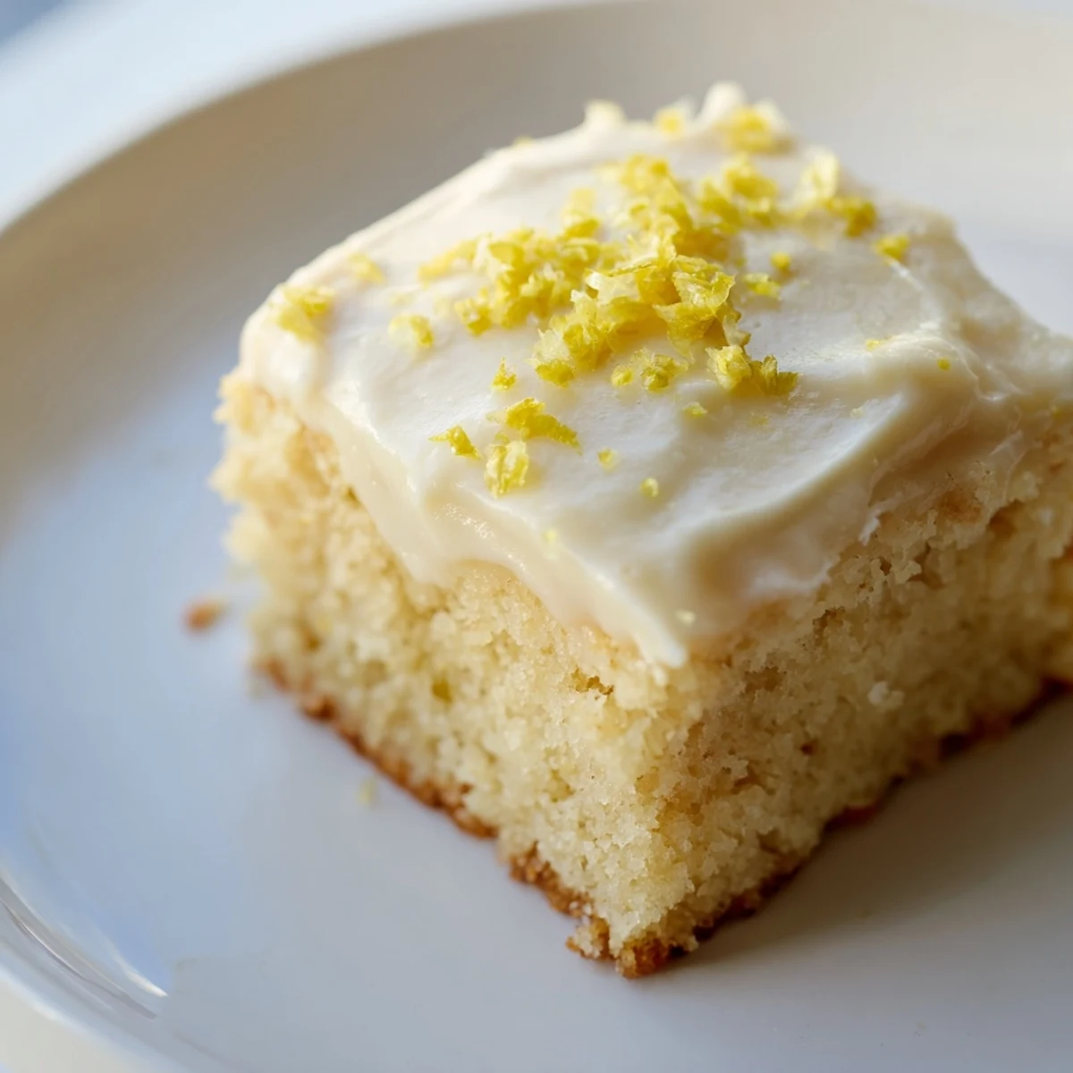 Lemon Cake with Frosting on a marble tray, garnished with lemon zest and a fresh lemon slice for a bright citrus look.