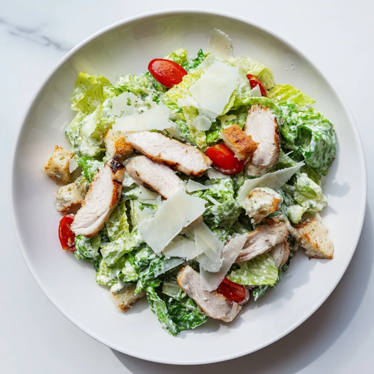 Grilled chicken slices rest atop crisp romaine lettuce and crunchy croutons in a Chicken Caesar Salad.