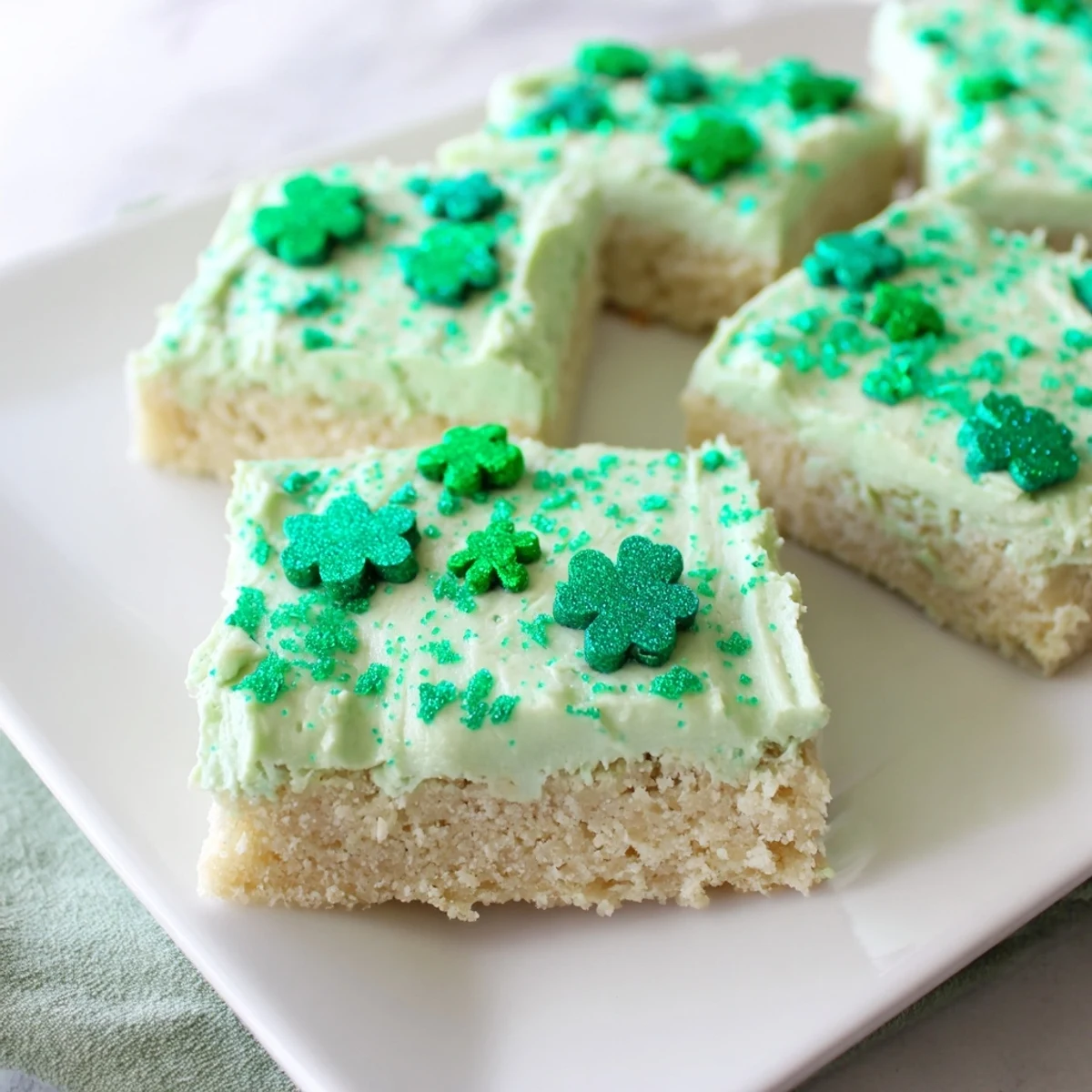 Four soft Shamrock Cookie Bars iced green and topped with festive shamrock sprinkles.