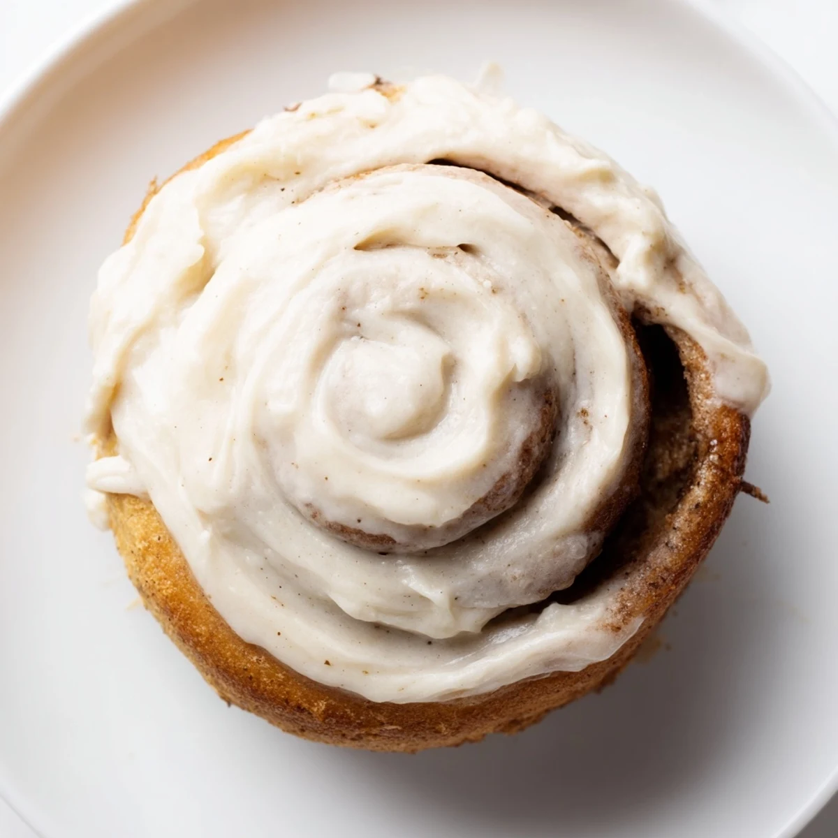 A close-up of warm Keto Cinnamon Buns with cream cheese icing melting down the spiraled dough.