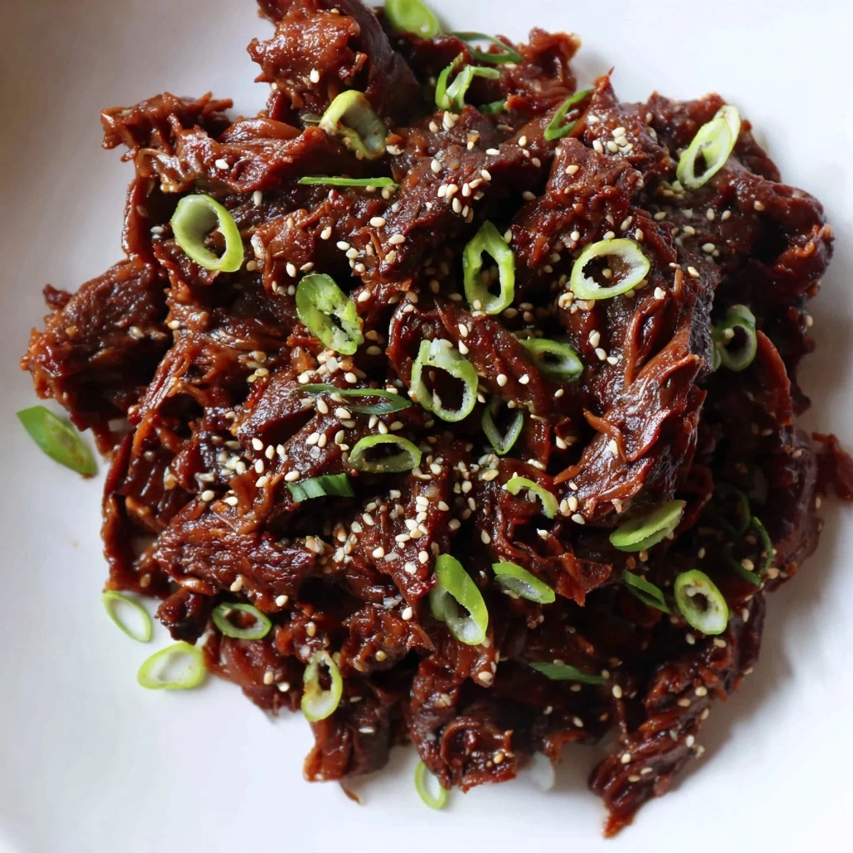 Slow cooker Korean beef simmering in a glossy, savory-sweet sauce with tender shredded meat ready to serve over steamed white rice.