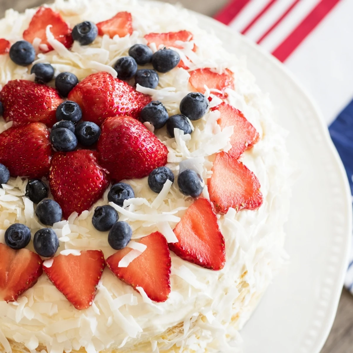 Moist slices of Pineapple Coconut God Bless America Cake displayed on a plate, garnished with fresh strawberries and blueberries.  