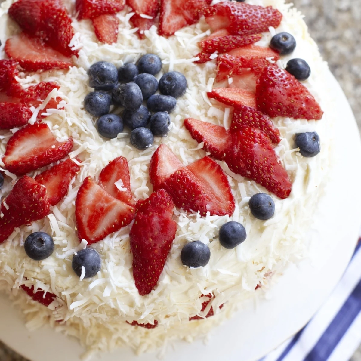 A close-up of Pineapple Coconut God Bless America Cake layered with cream cheese frosting, topped with patriotic red and blue berries.  