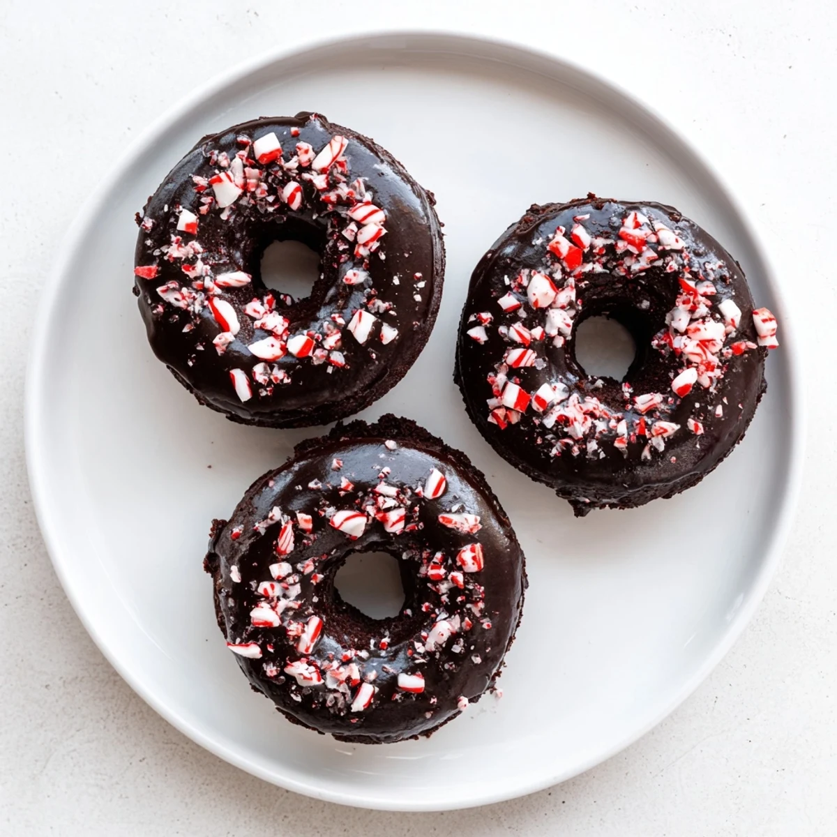 Enjoy soft, chewy Chocolate Peppermint Mochi Donuts arranged on a white ceramic plate with a glass of milk.