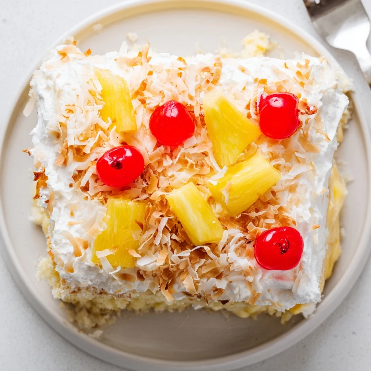 Hawaiian Poke Cake with fluffy whipped topping, toasted coconut flakes, and bright red maraschino cherries