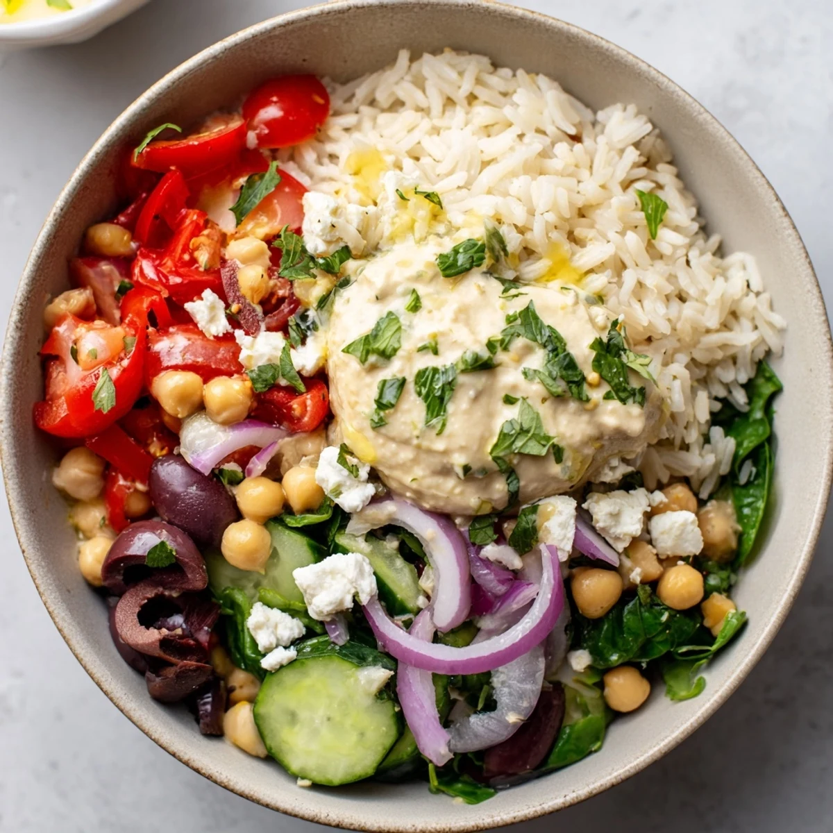Colorful Mediterranean rice bowl with fluffy rice, crisp vegetables, and creamy hummus drizzled with lemon-tahini dressing