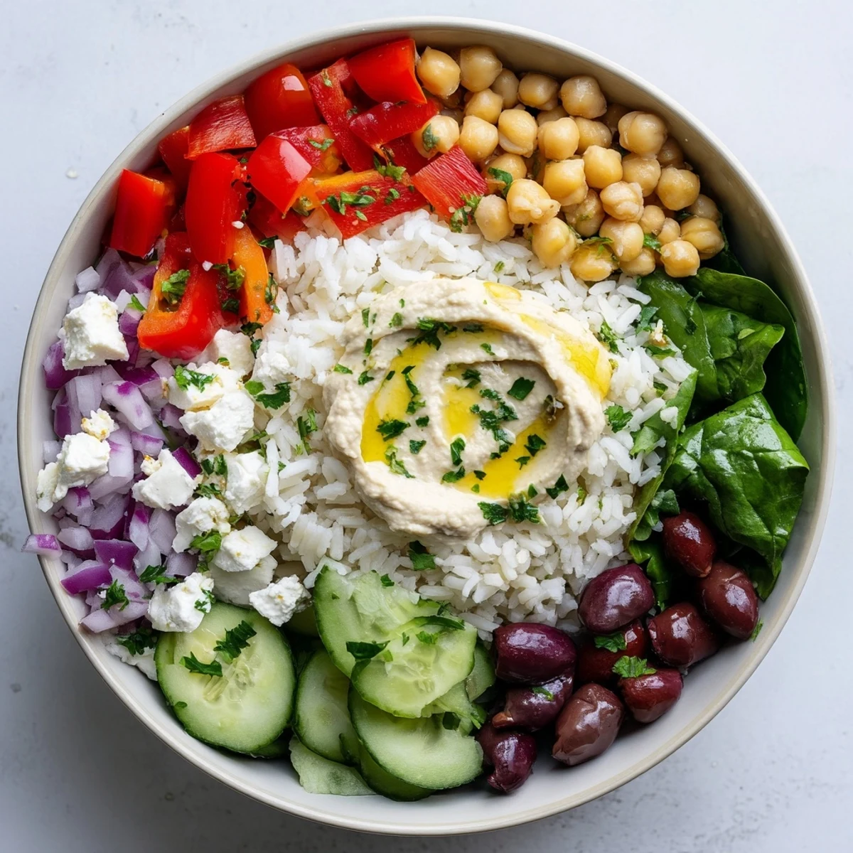 Vegetarian Mediterranean rice bowl topped with zesty tahini dressing, cherry tomatoes, cucumber, and crumbled feta cheese