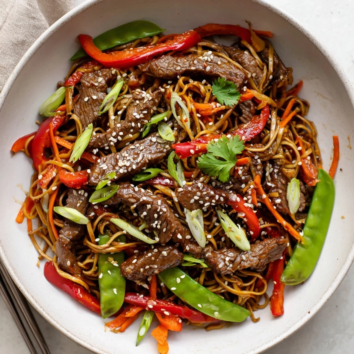 Steak strips coated in caramelized sticky glaze served over chewy noodles with bell peppers, carrots, and snap peas