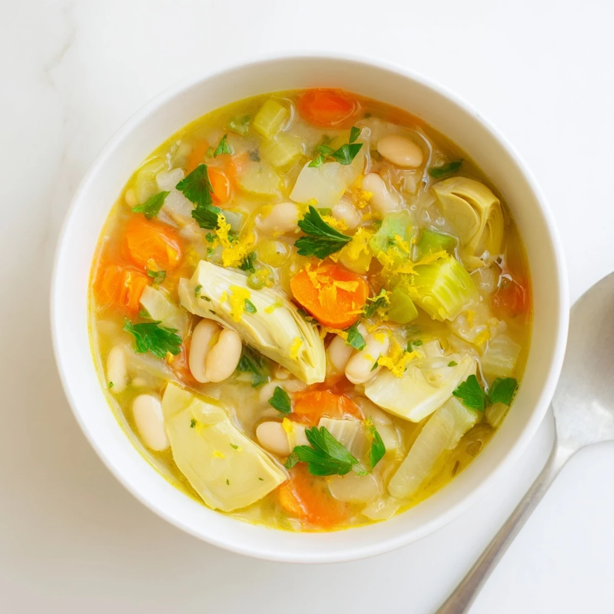 Creamy bowl of Lemony Tuscan Artichoke Soup garnished with fresh parsley and lemon wedges