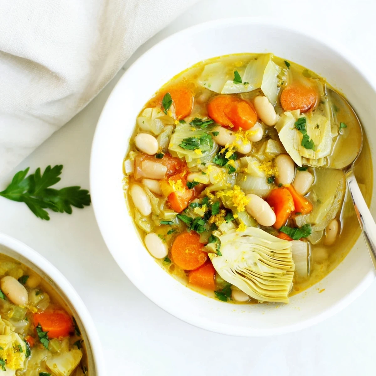 Rustic white ceramic crock filled with chunky vegetable and artichoke soup with parsley sprinkles
