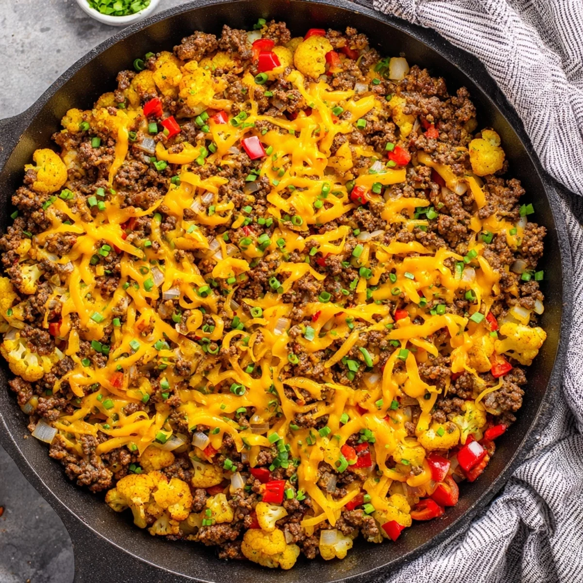 Hearty skillet meal featuring tender cauliflower florets mixed with seasoned ground beef and vibrant red peppers