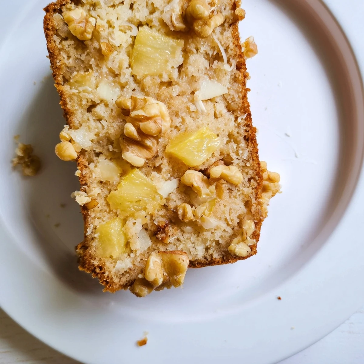 Golden slice of coconut pineapple banana bread topped with shredded coconut on a wooden board