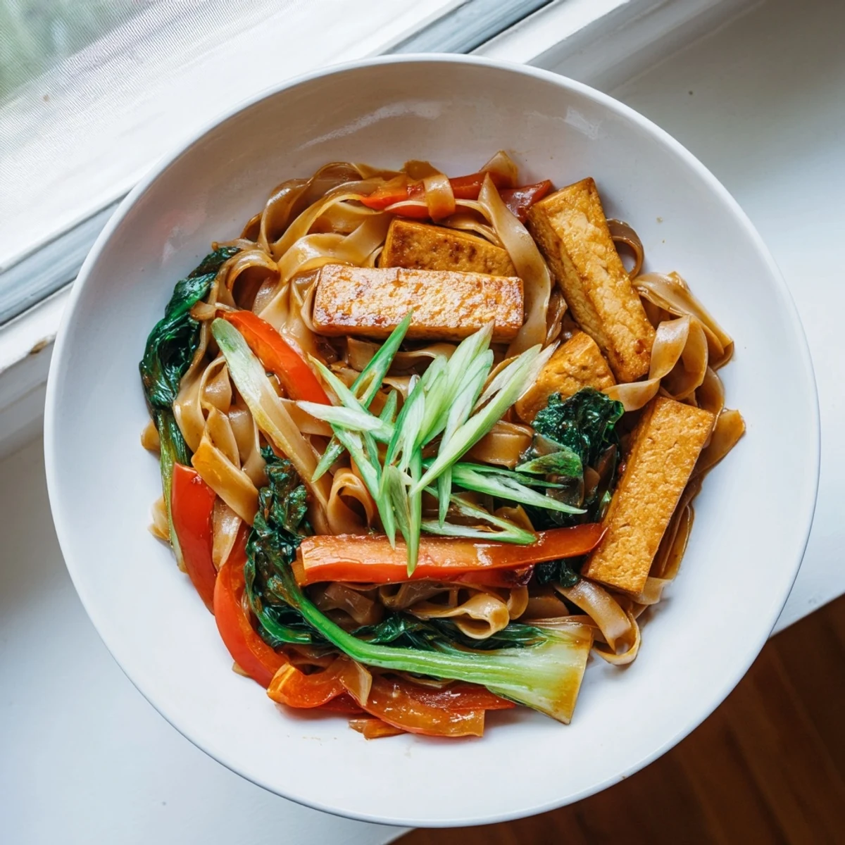 Close-up of Vegan Pad See Ew noodle dish garnished with fresh green onions and lime wedges