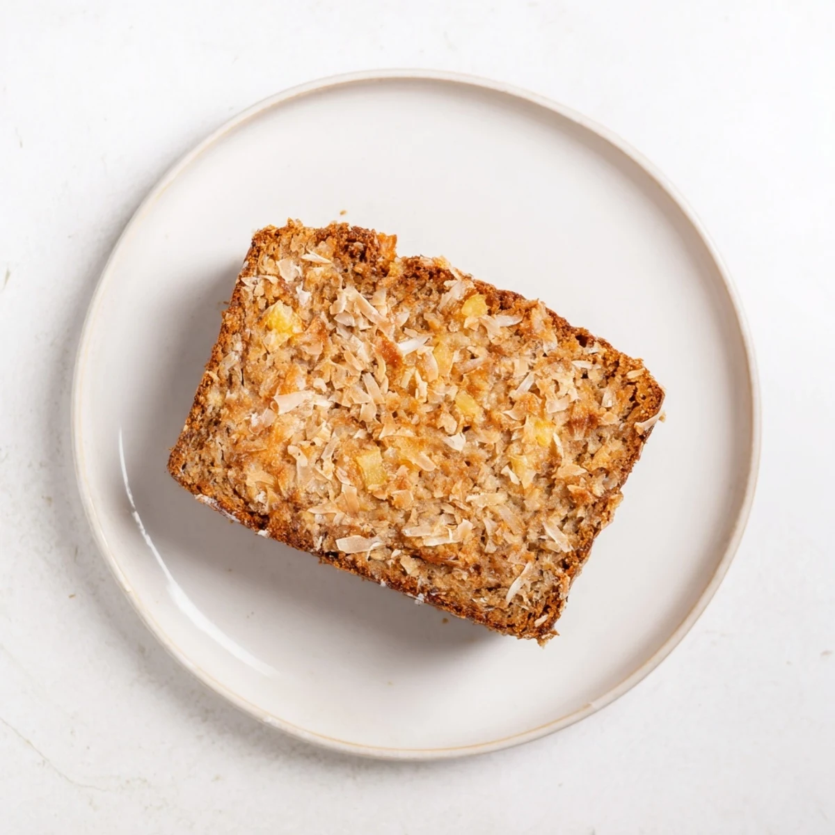 Golden slice of cozy pineapple coconut bread topped with shredded coconut on a wooden board