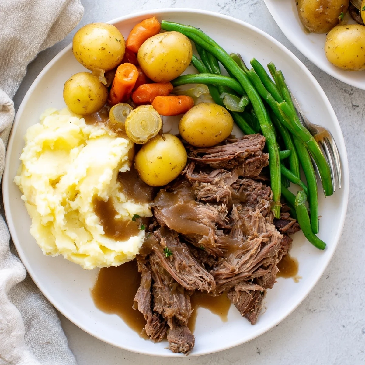 Fork-tender Southern style pot roast slices served over braised vegetables with creamy mashed potatoes and savory beef gravy