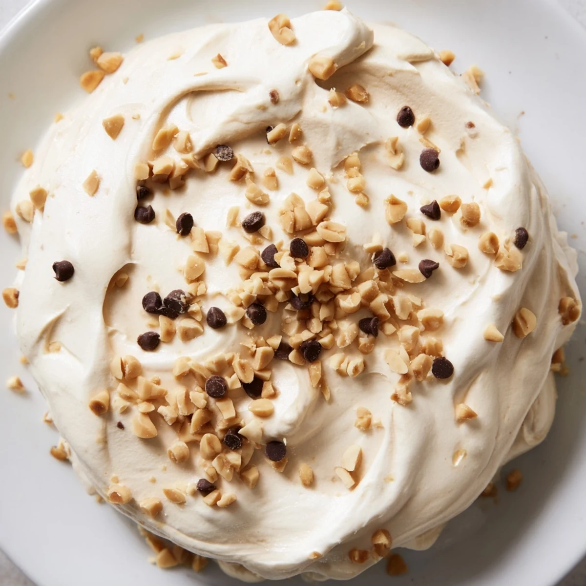 Creamy peanut butter and Cool Whip mousse topped with chocolate chips and chopped roasted peanuts in a clear glass bowl