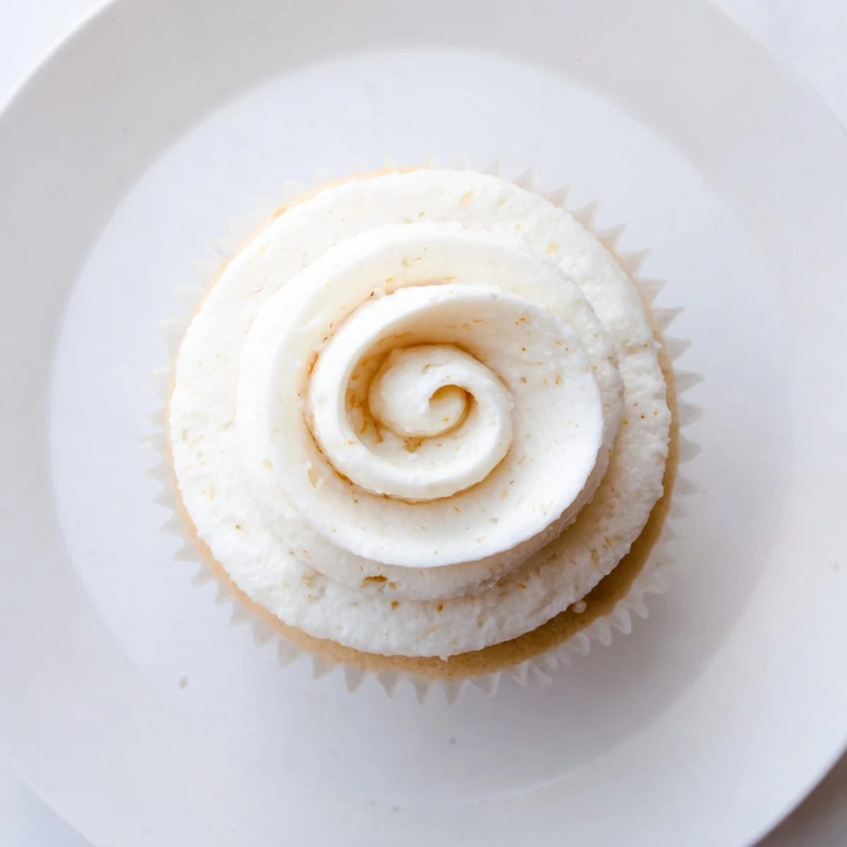 Golden vanilla cupcakes topped with fluffy swirls of creamy white buttercream frosting on a decorative plate