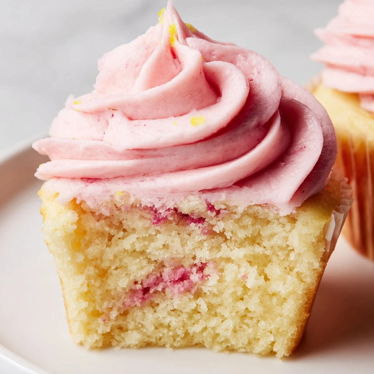Golden strawberry lemonade cupcakes with pink buttercream swirled high on white plates