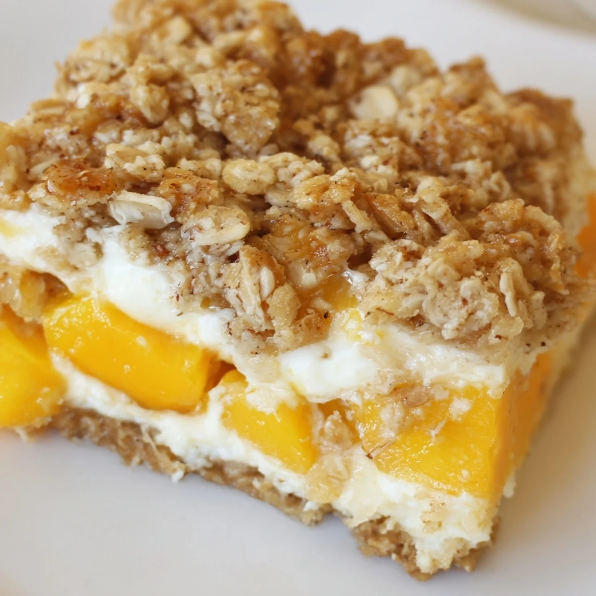 Golden Peaches And Cream Crumble Bars with buttery oat topping on a rustic white plate