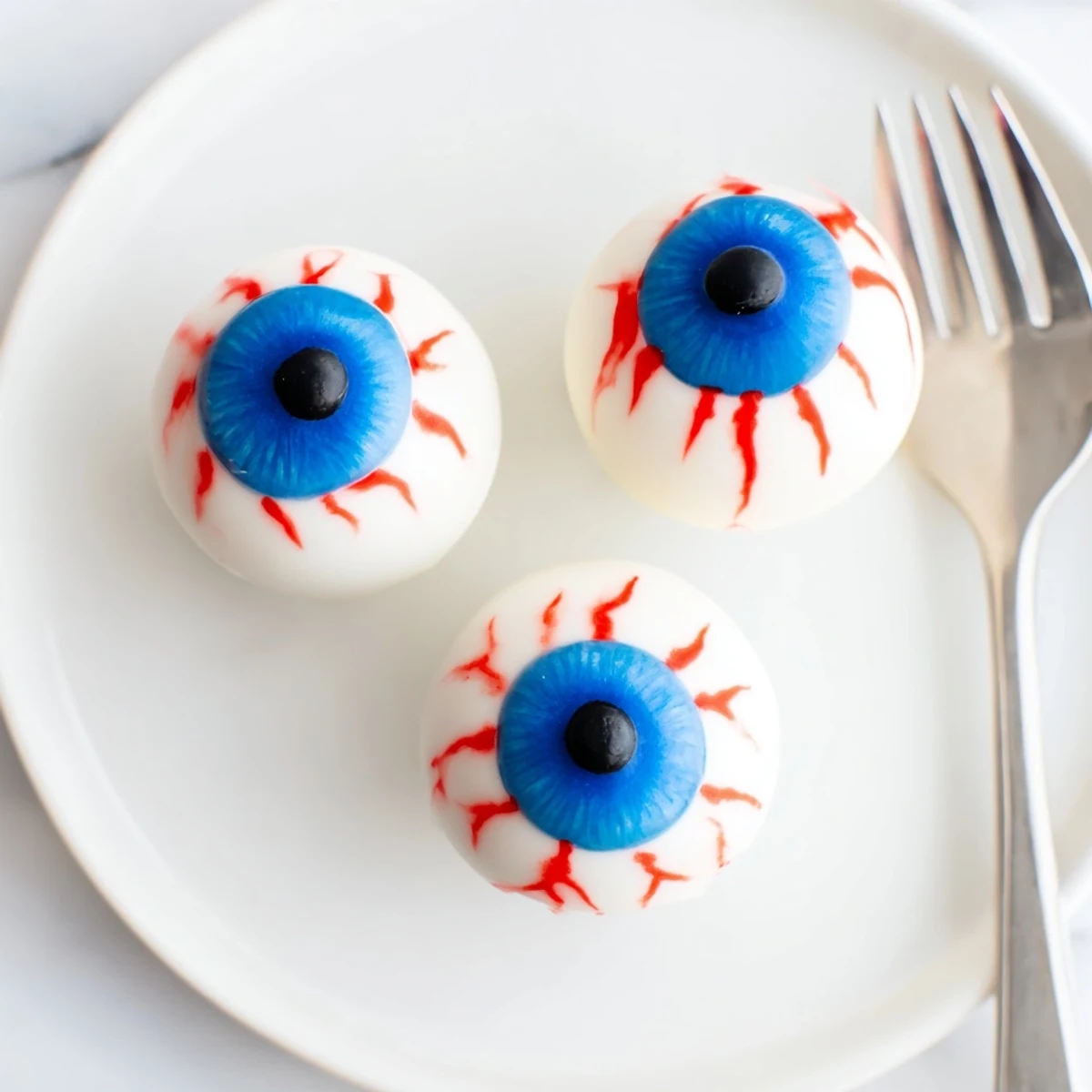 Close-up of glossy white chocolate-coated Halloween Cake Eyeballs showing blue pupils and bloodshot lines