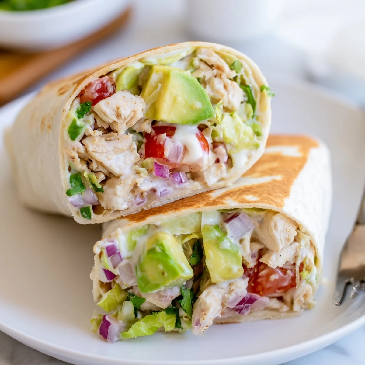 Handheld Chicken Avocado Ranch Burritos halved, zesty dressing drips beside cilantro.