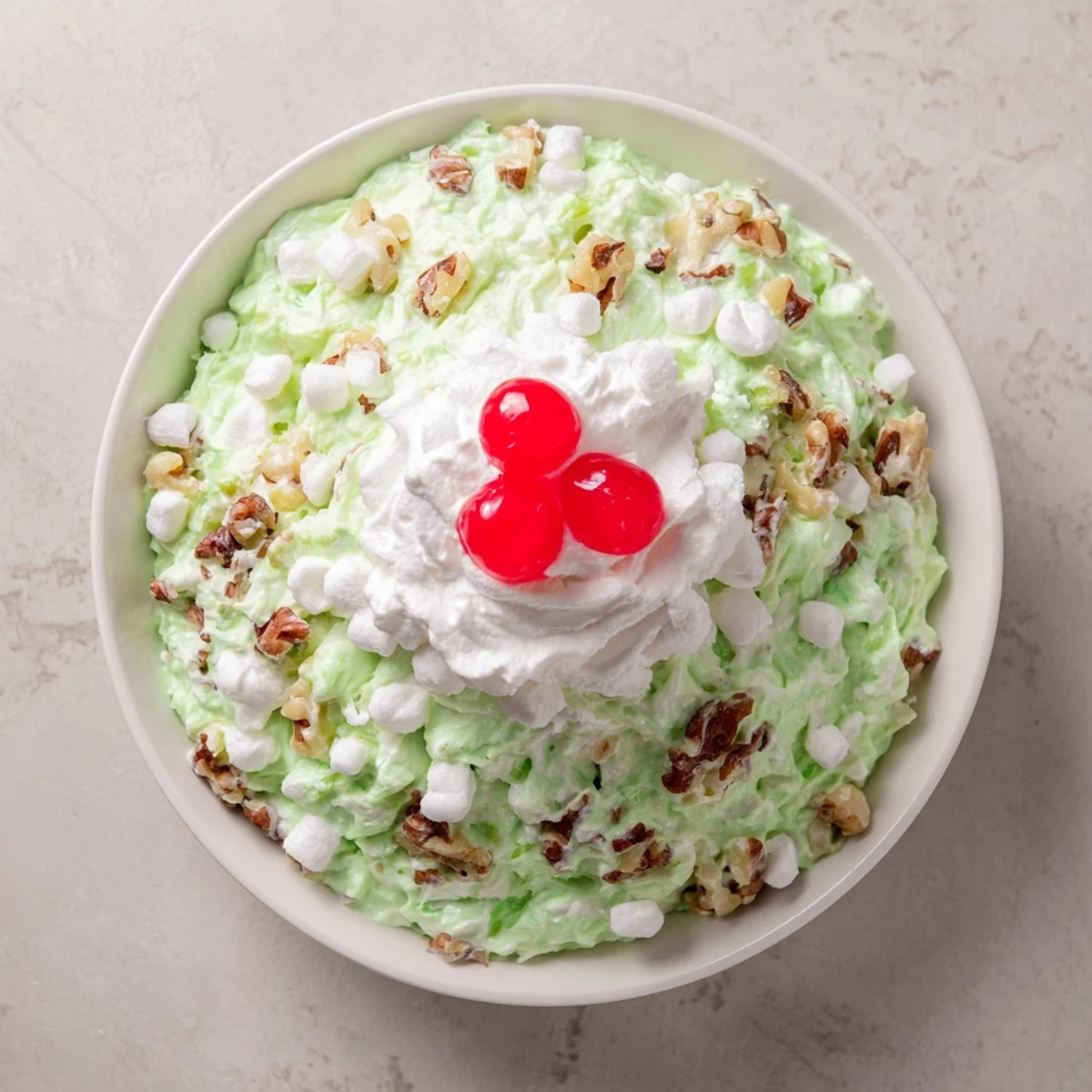 Creamy Watergate Salad recipe topped with dollops of whipped cream and maraschino cherries on a vintage holiday table setting