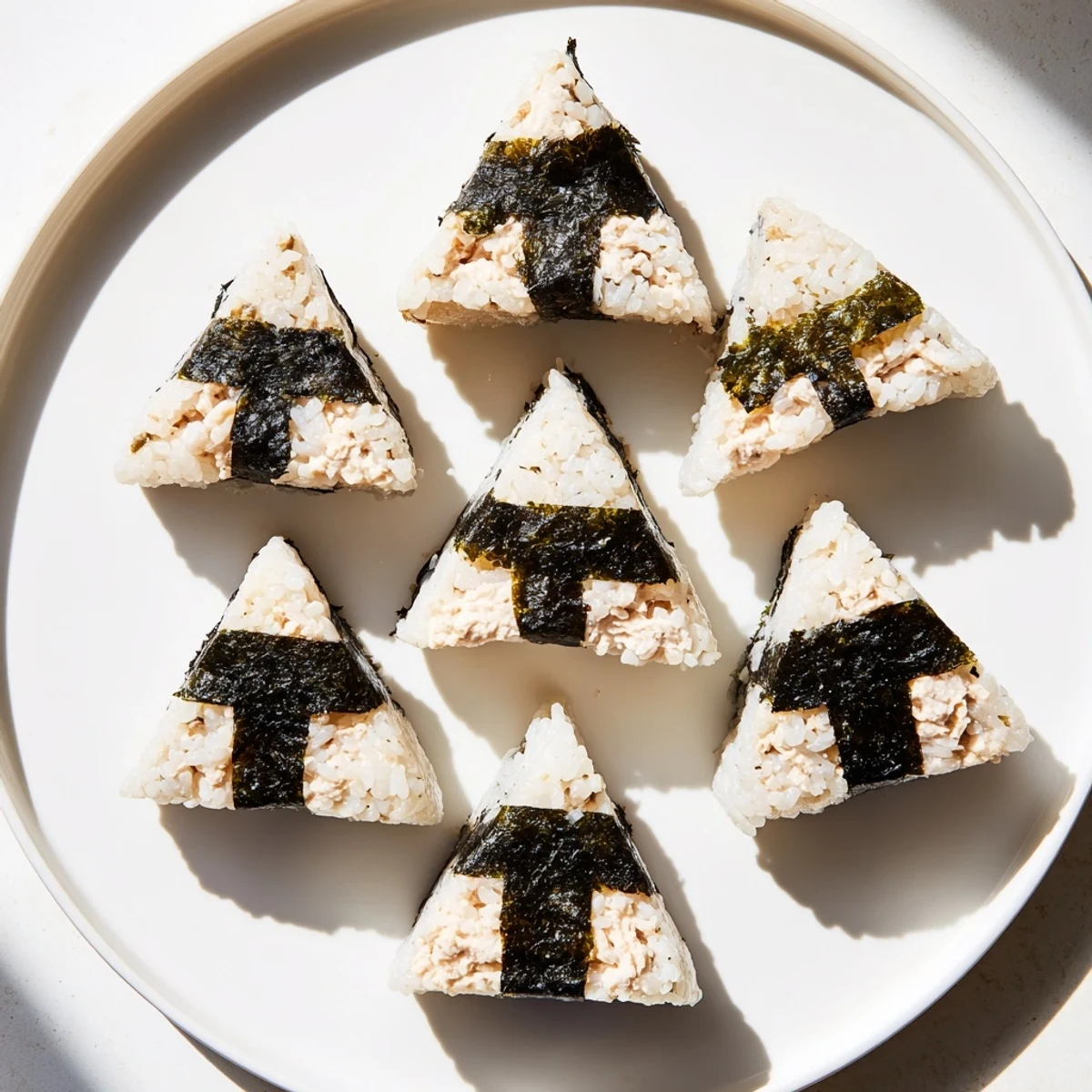 Handheld triangular tuna mayo onigiri rice ball wrapped in crisp nori seaweed strip