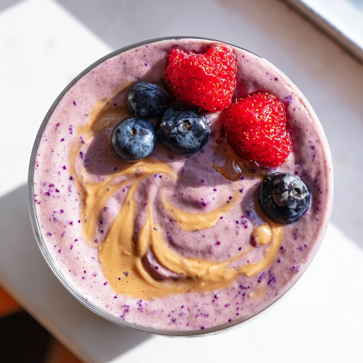 Thick purple peanut butter berry smoothie topped with fresh strawberries in a glass