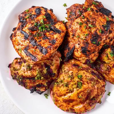 Juicy Cajun Spiced Grilled Chicken Thighs served with rice and corn, garnished with fresh parsley for a flavorful meal.