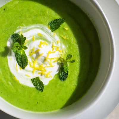A close-up view of Spring Pea Soup with Mint and Crème Fraîche, featuring a velvety texture and a dollop of tangy crème fraîche.  