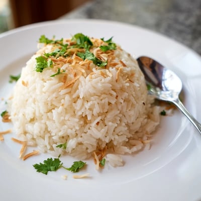 Steaming bowl of coconut rice served alongside Thai curry in rustic dishware